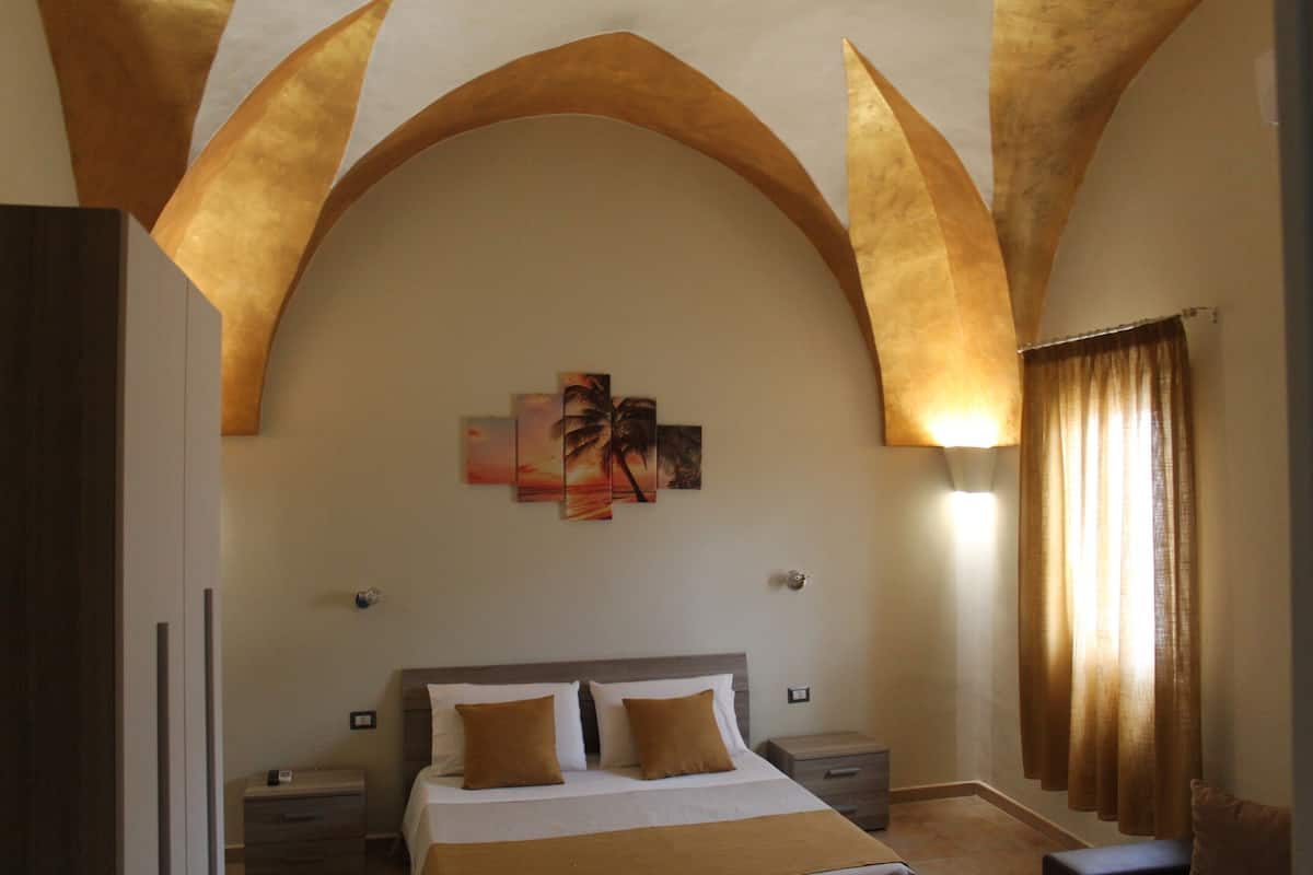 A bedroom with a large bed, two bedside tables, a nightstand, and a wall-mounted artwork.
