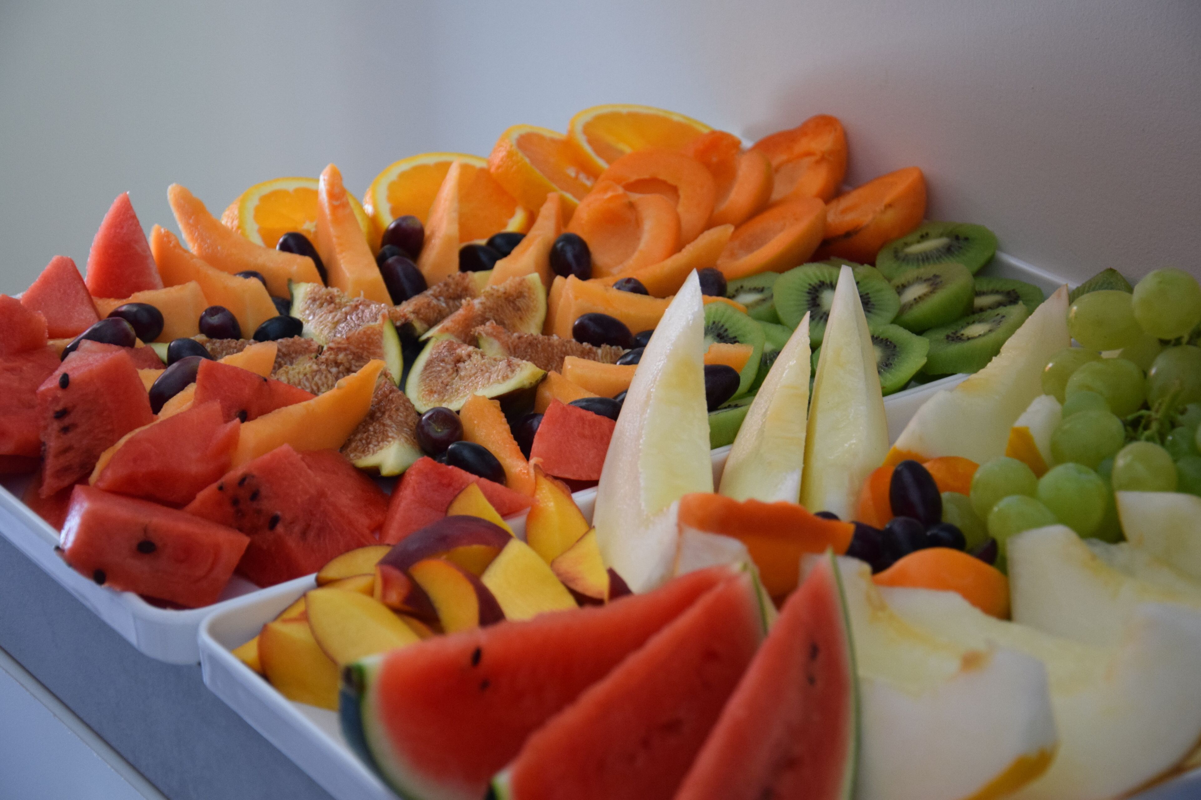 A tray of assorted fruits including watermelon, oranges, grapes, and kiwi.