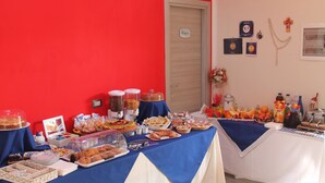 Ein Büfett mit verschiedenen Speisen und einer Kaffeestation, vor einer roten Wand mit einer Tür und einigen Wanddekorationen.