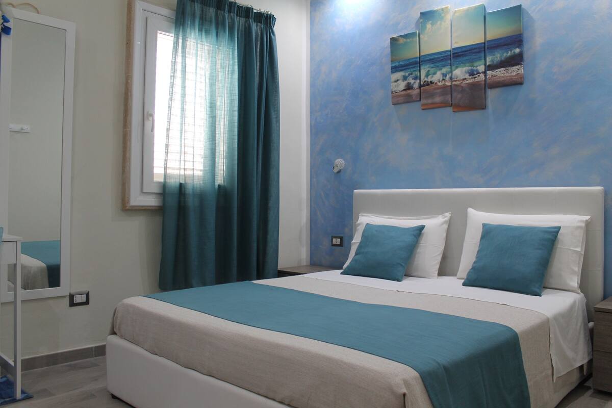 A bedroom with a bed, a nightstand, and a wall-mounted painting of a beach scene.