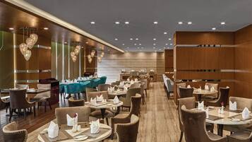 A spacious restaurant with multiple tables and chairs, wooden paneling, and modern lighting fixtures.