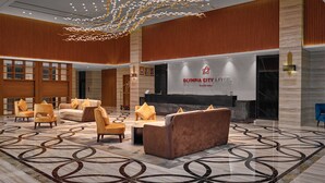 Een moderne lobby met een receptiebalie, een zithoek en een decoratieve plafondlamp.