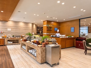 Eine moderne Hotelhalle mit einem Frühstücksbereich, einem Koch bei der Arbeit und einer Rezeption.