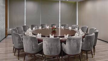 A conference room with a round table, grey upholstered chairs, and a vase with red flowers.