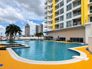 A swimming pool with a surrounding walkway, palm trees, and a modern building with balconies in the background. - TUI SUNEO Olympia Phnom Penh (Phnom Penh)