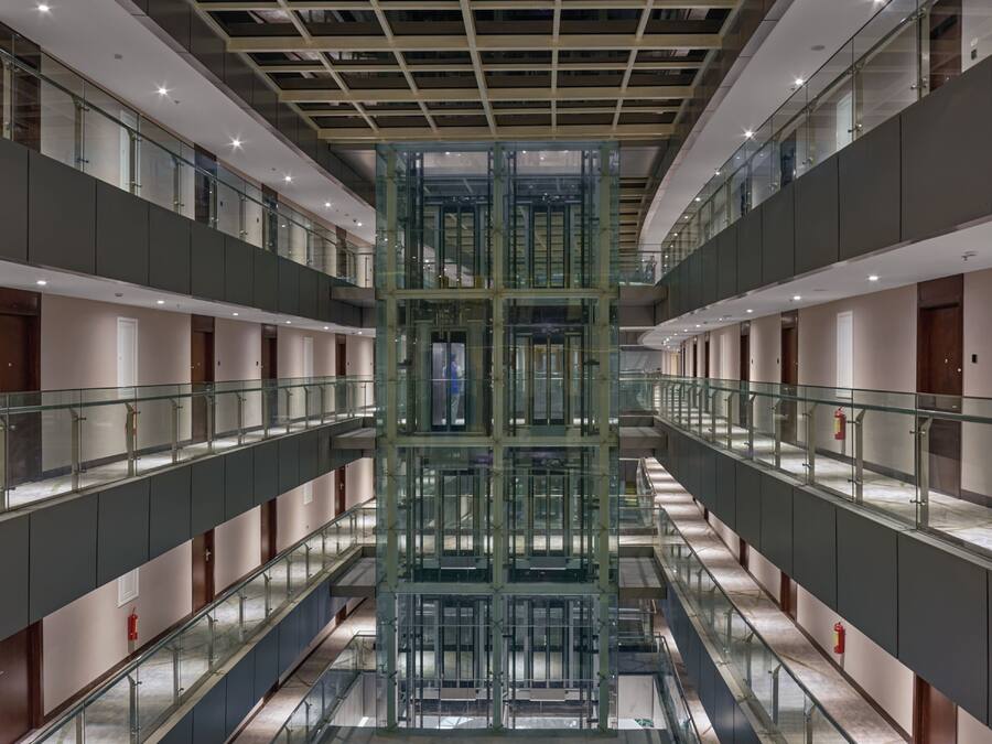 Un edificio moderno con varios pisos, barandas de vidrio y un eje central para ascensor.