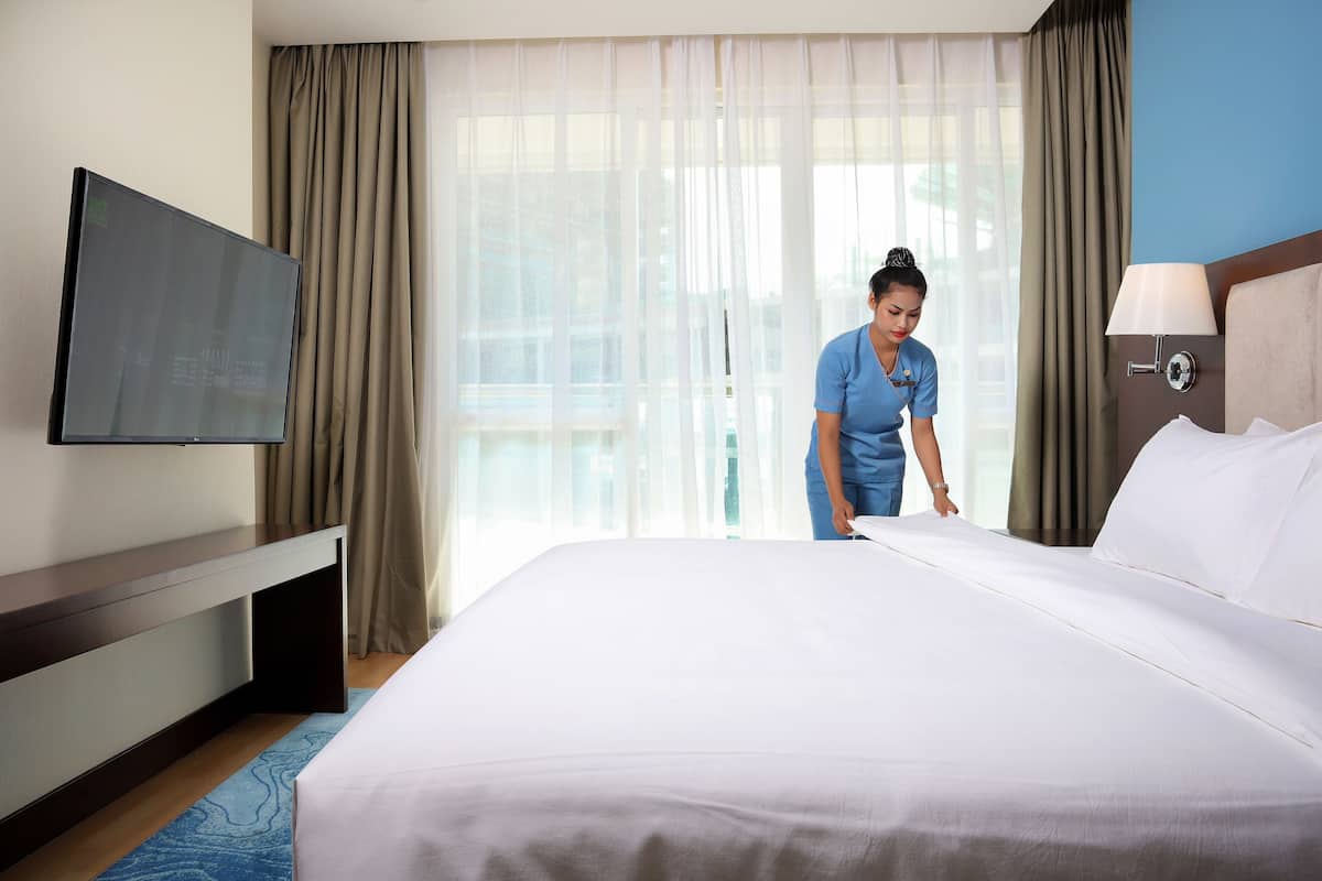 A hotel room with a bed, a flat-screen TV mounted on the wall, a desk, and a lamp.