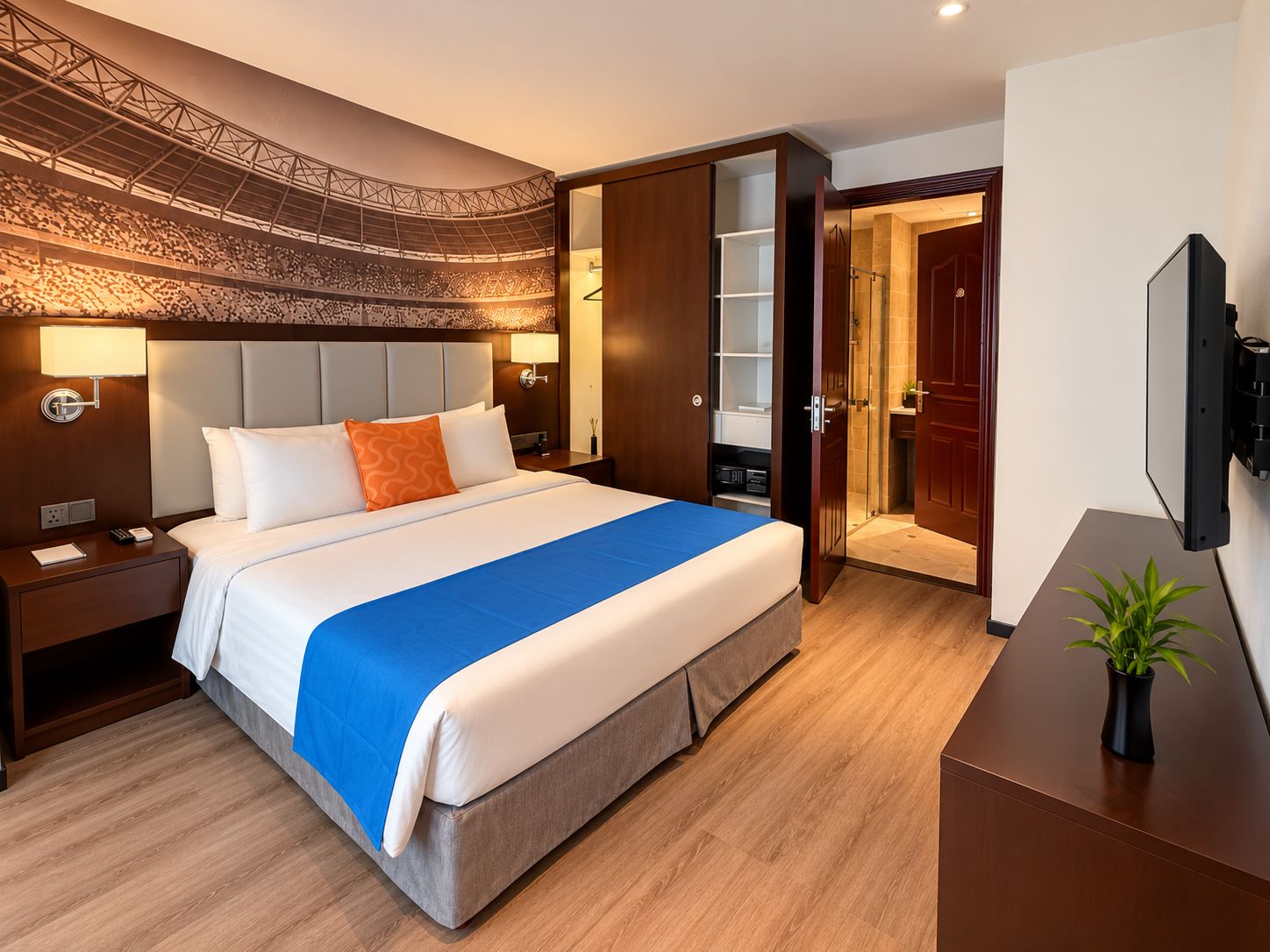 Habitación de hotel con una cama grande, mesitas de noche, televisión y un baño visible a través de una puerta abierta.