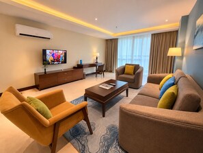 A modern hotel room with a flat-screen TV, a sofa set, a coffee table, and a desk with a lamp. - TUI SUNEO Olympia Phnom Penh (Phnom Penh)