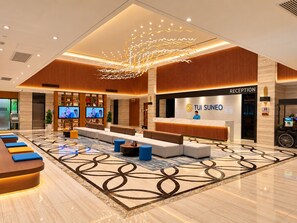 A modern hotel lobby with a reception desk, seating area, and a large TV screen. - TUI SUNEO Olympia Phnom Penh (Phnom Penh)