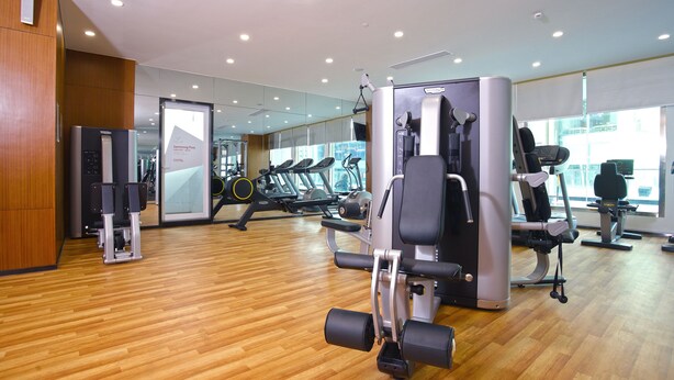A modern gym with wooden flooring, various exercise machines, and a large mirror reflecting the space. - Olympia City Hotel by Dara (Phnom Penh)