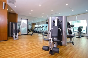 Un gimnasio moderno con suelo de madera, diversas máquinas de ejercicio y un espejo grande que refleja el espacio.