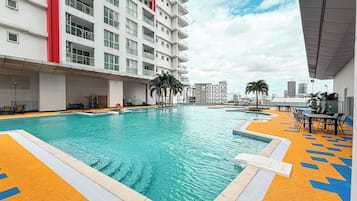 Una piscina con solarium empedrado, rodeada por un edificio de varios pisos con balcones.