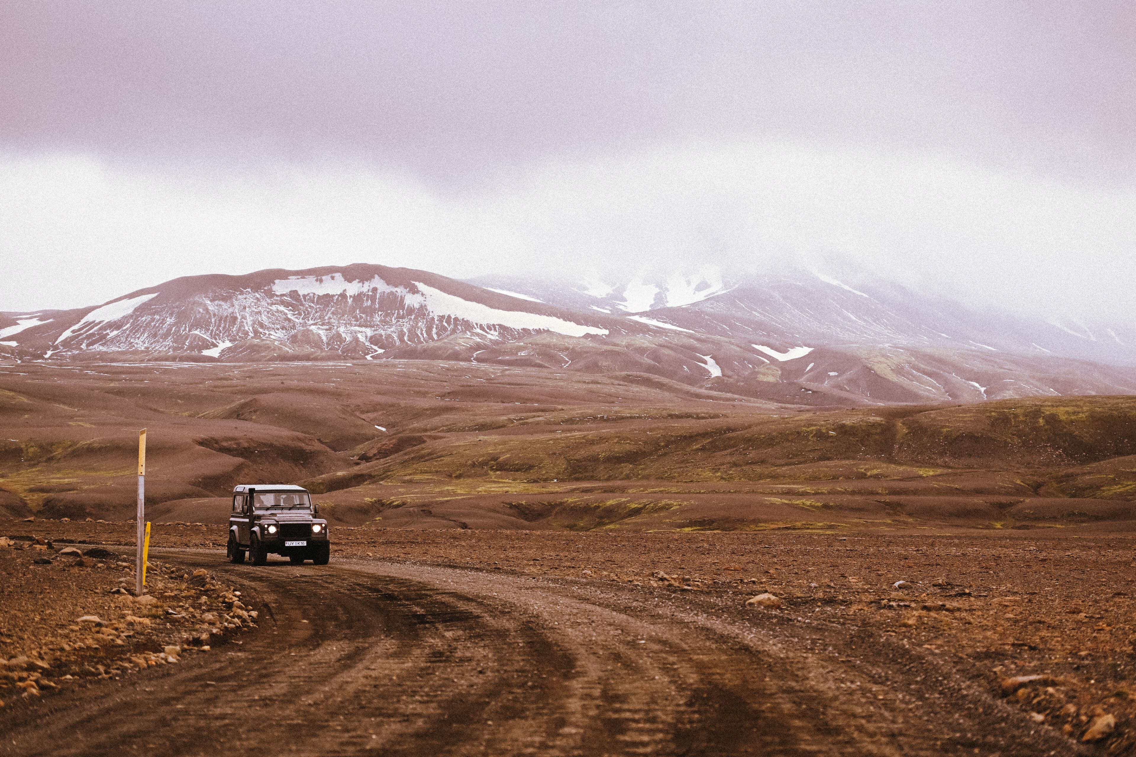 A vehicle on a dirt road with a mountainous backdrop.