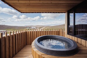 Una terraza de madera con un jacuzzi y vistas a un paisaje rural.