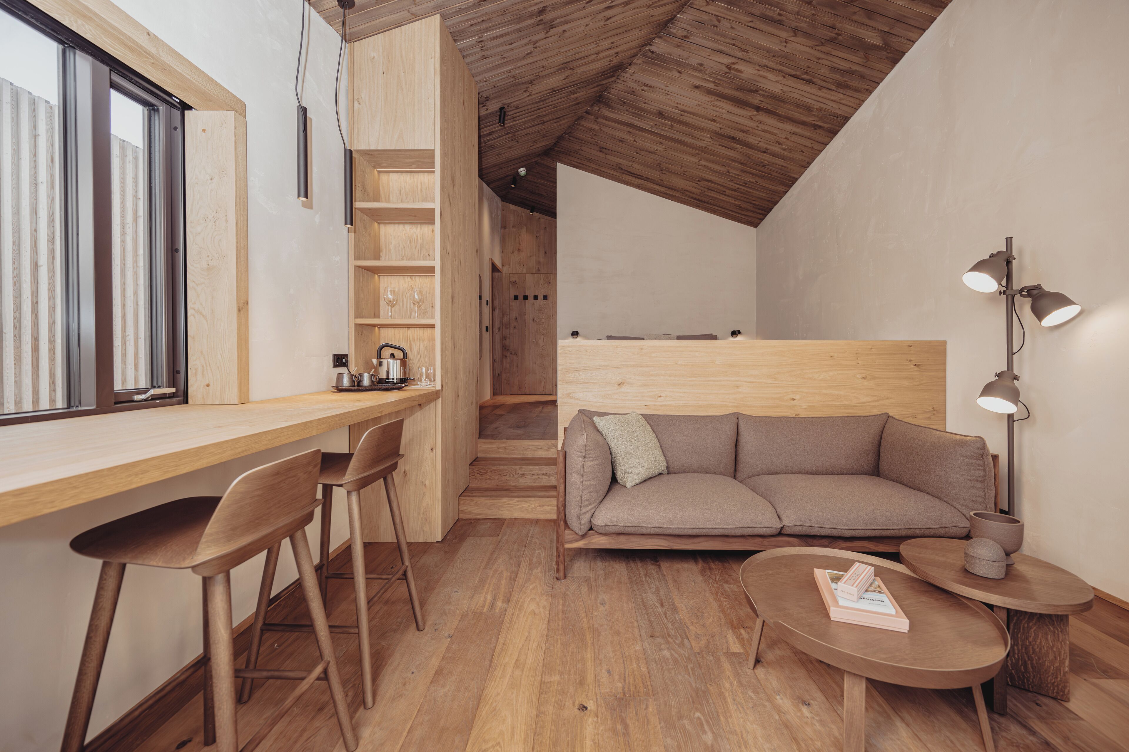 A modern, open-plan living and dining area with wooden flooring, a sofa, a coffee table, and a desk with chairs.