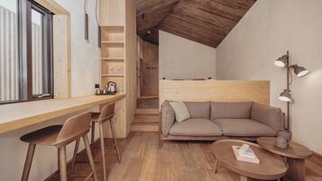 A modern, open-plan living and dining area with wooden flooring, a sofa, a coffee table, and a desk with chairs.