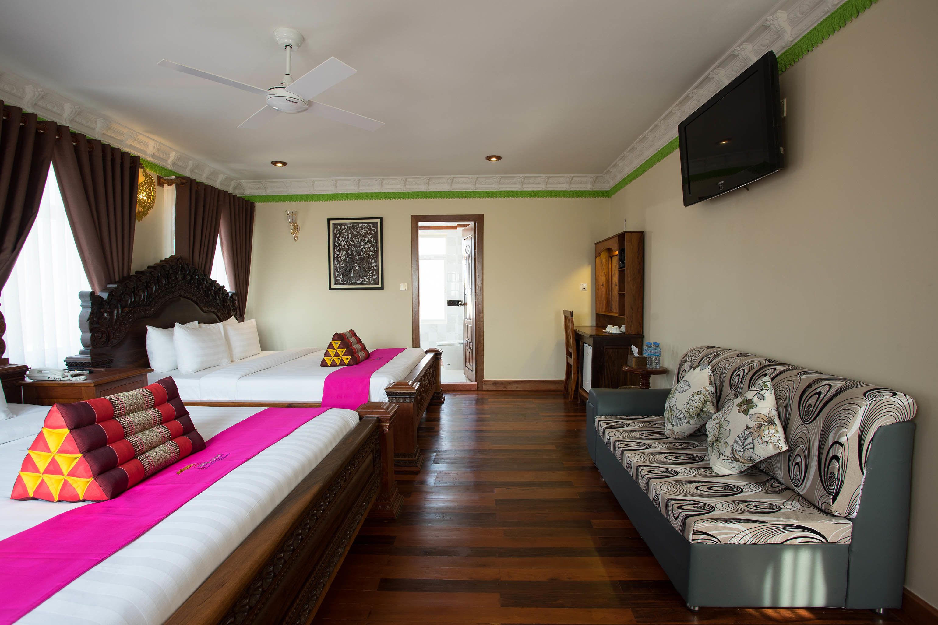 A hotel room with two beds, a sofa, a television, and a ceiling fan.