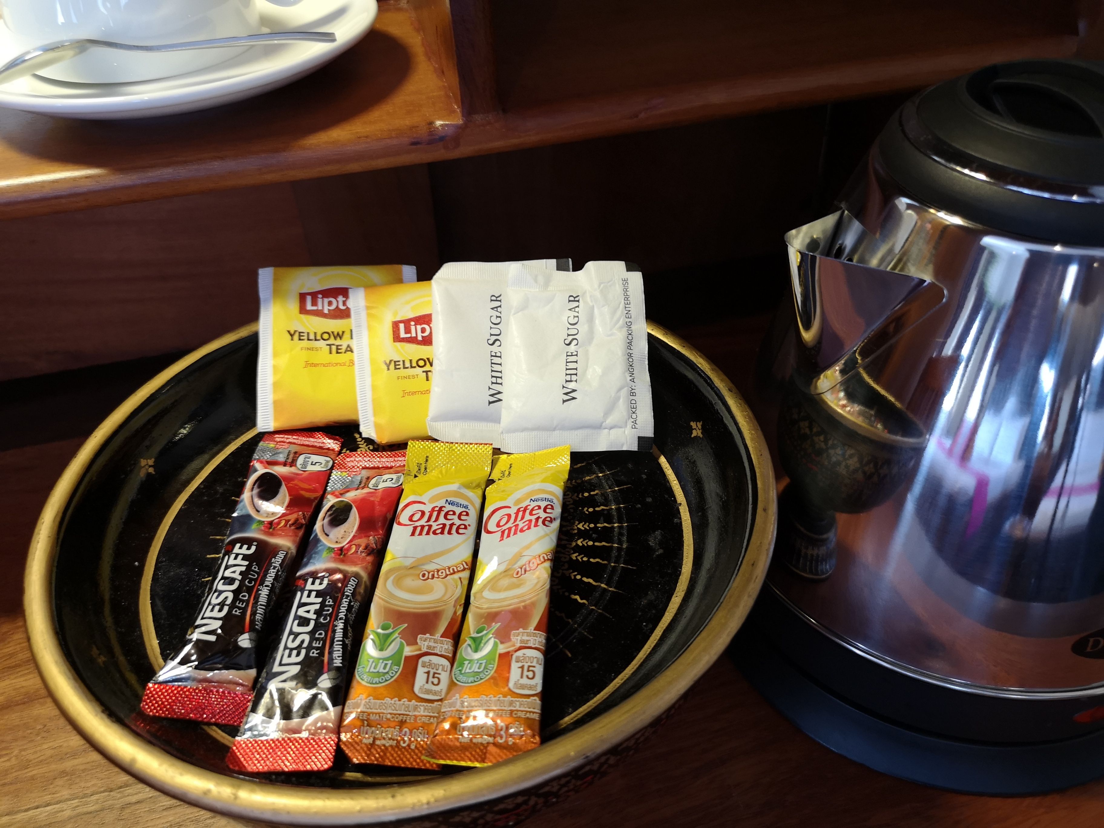 A tray with various coffee and tea packets, a coffee pot, and a spoon on a table.