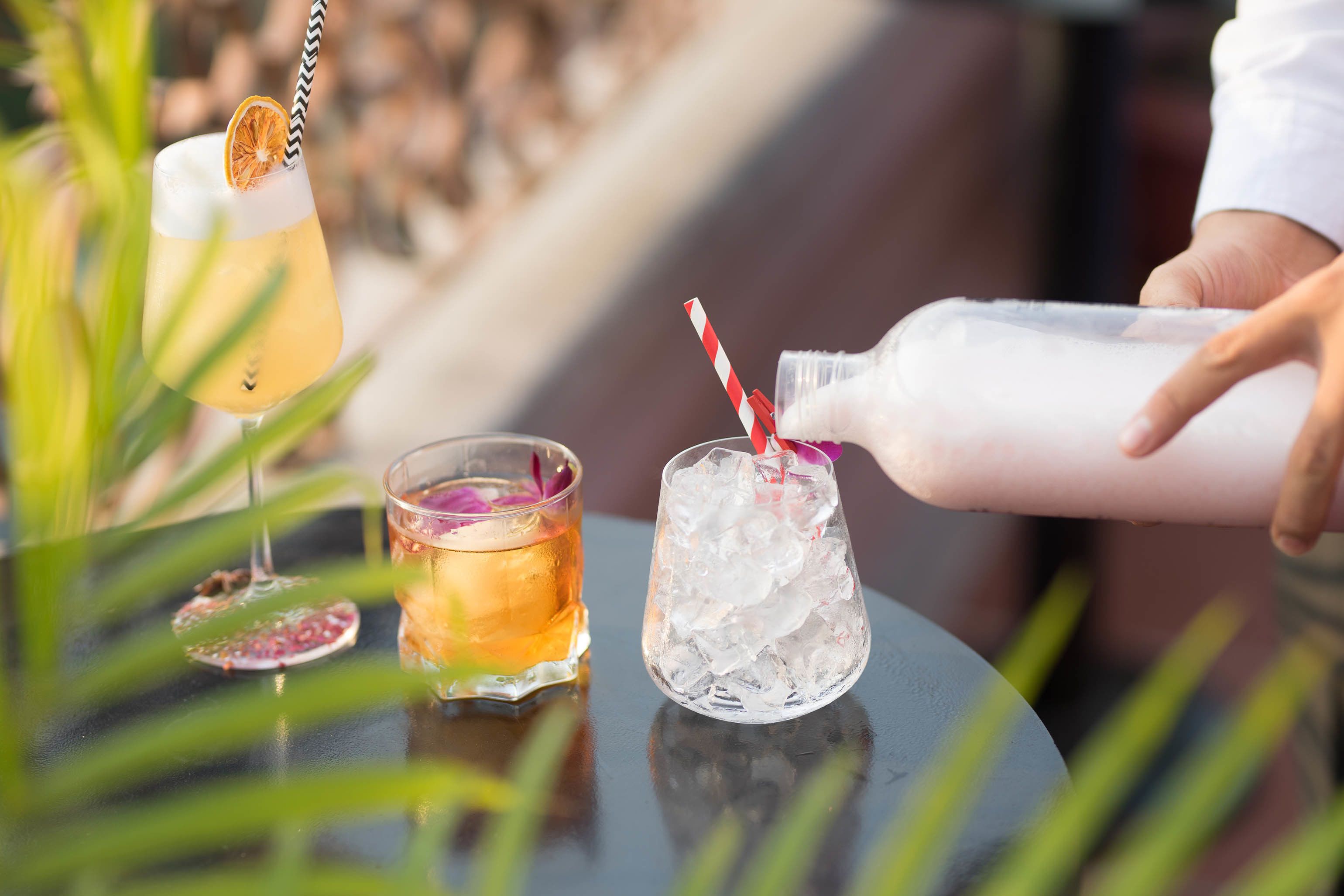A cocktail being poured into a glass with ice and a striped straw.