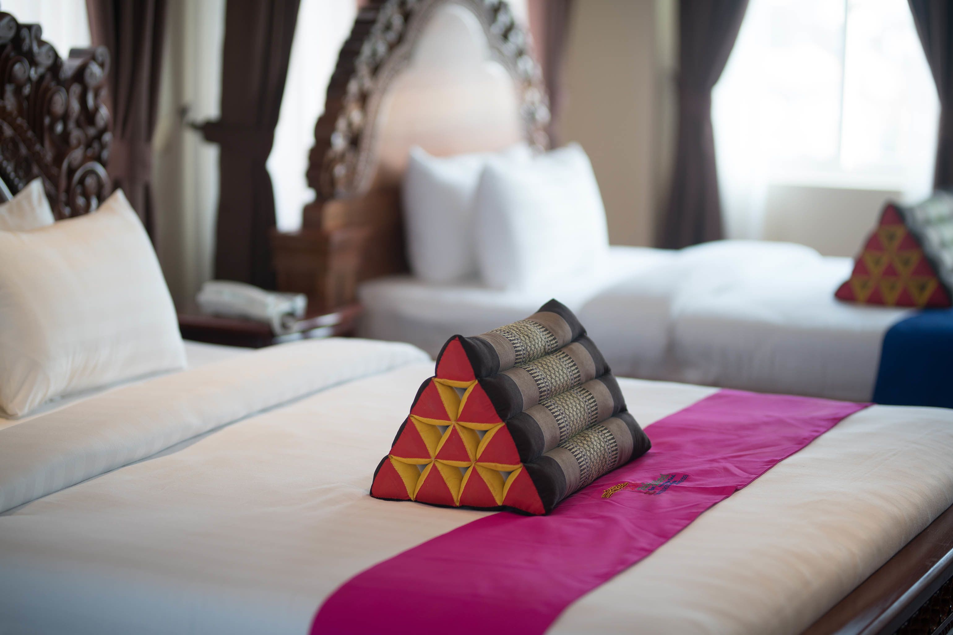 A hotel room with two beds, each with white linens and decorative pillows.