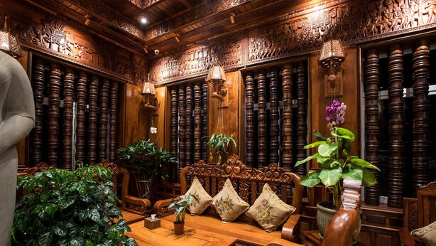 Un interior de madera tradicional con detalles tallados, un sofá de madera con cojines y una planta en maceta.