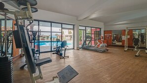 A gym with various exercise equipment, large windows, and a view of an outdoor area. - Treebo Premium Blue Mountain Country Club And Resort (Siliguri)