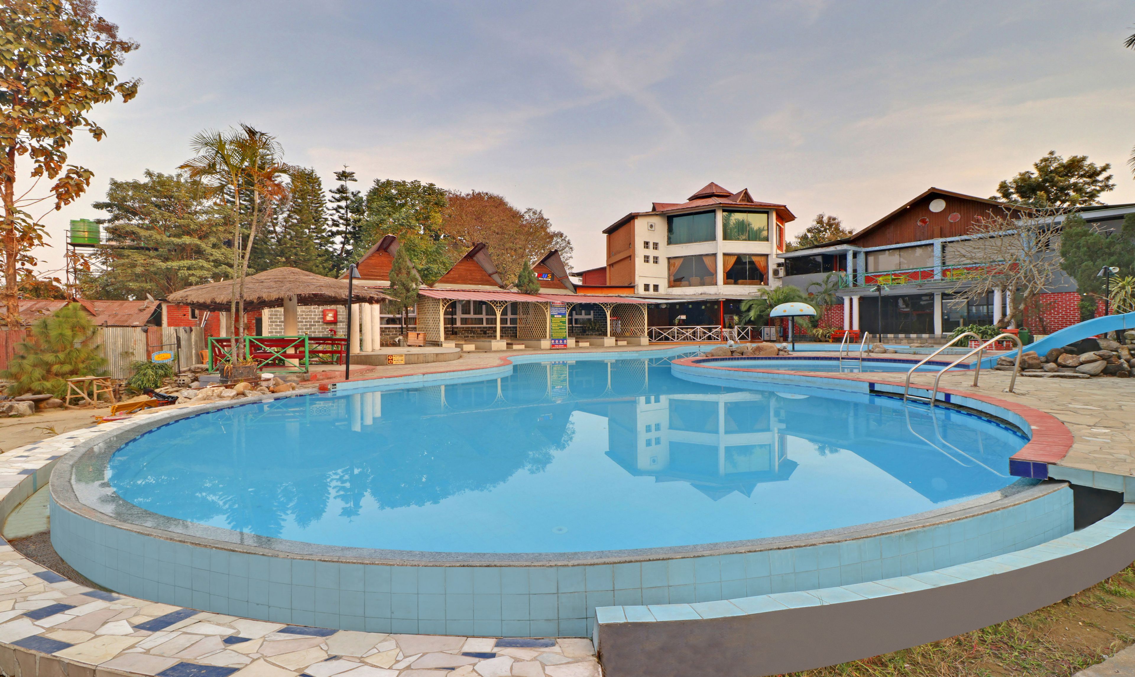 Una piscina con bordes de azulejos, rodeada de edificios con diversos estilos arquitectónicos, incluyendo una construcción de varios pisos con techo rojo.