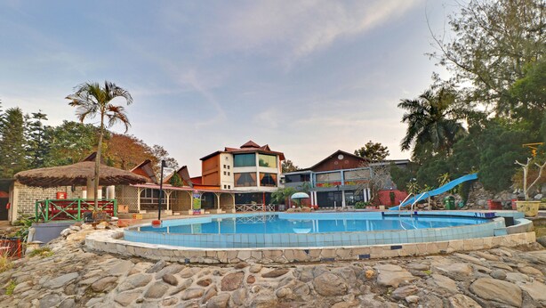 A swimming pool surrounded by stone tiles, with a building in the background. - Treebo Premium Blue Mountain Country Club And Resort (Siliguri)