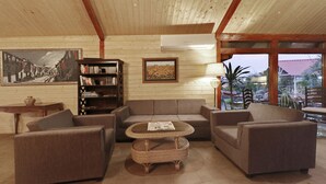 A cozy living room with a sofa set, a wicker coffee table, a bookshelf, and a painting on the wall. - Treebo Premium Blue Mountain Country Club And Resort (Siliguri)
