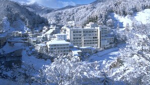 A snow-covered town with buildings, including a multi-story hotel with a central courtyard and a mountain backdrop. - Tsuchiyu Onsen MUKAITAKI (Fukushima)