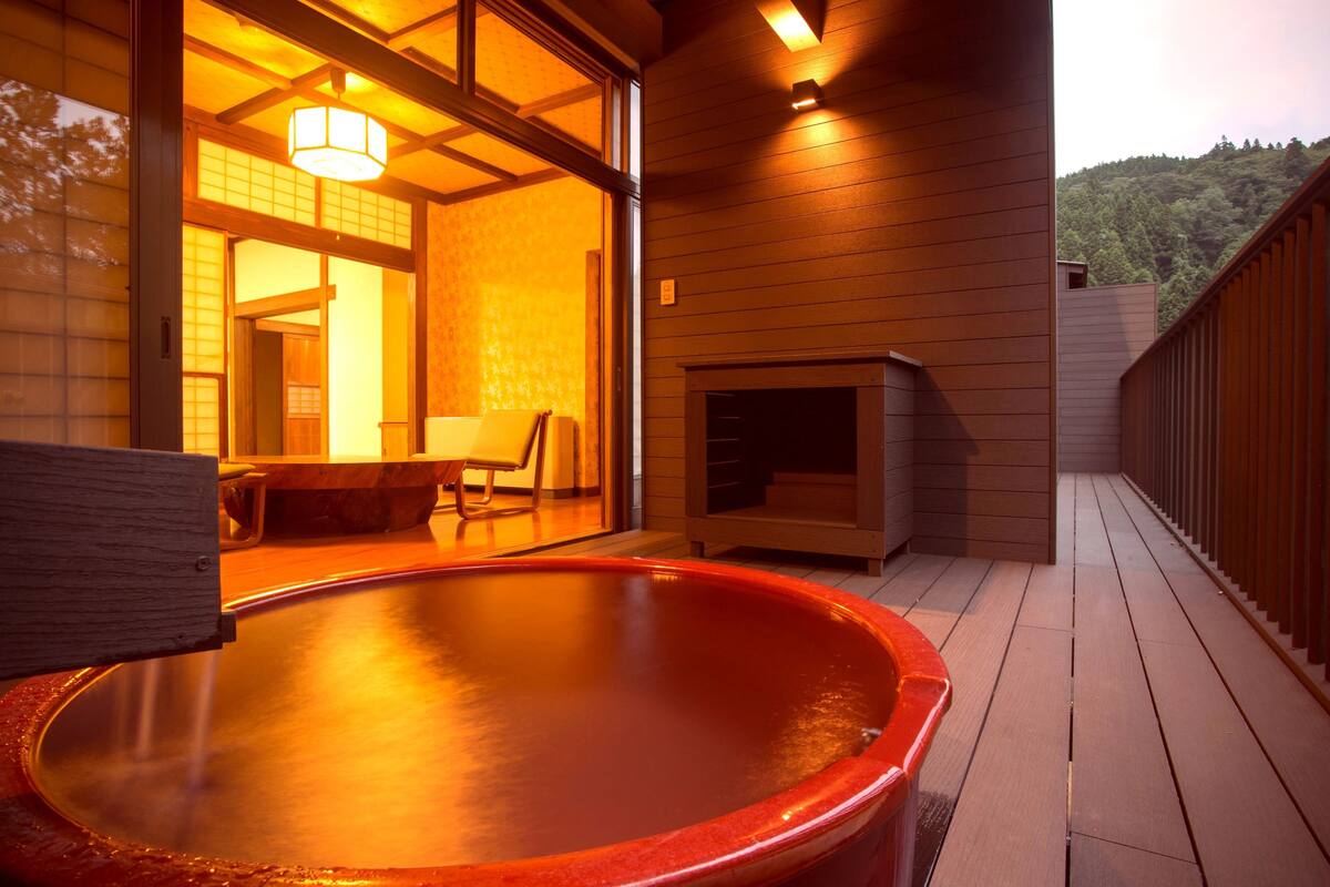 Un jacuzzi en una terraza de madera con vistas a un interior japonés tradicional.