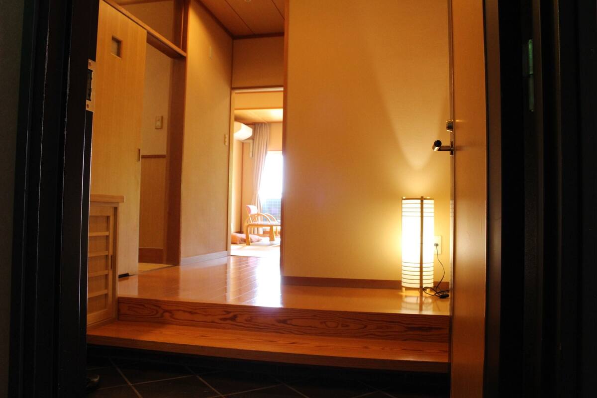 Un pasillo con piso de madera, una lámpara y una puerta que da a otra habitación.