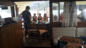 Ruokailutila, jossa on ruokapöytä katettuna, puiset tuolit ja buffetpöytä, jossa on tarjolla erilaisia ruokia.