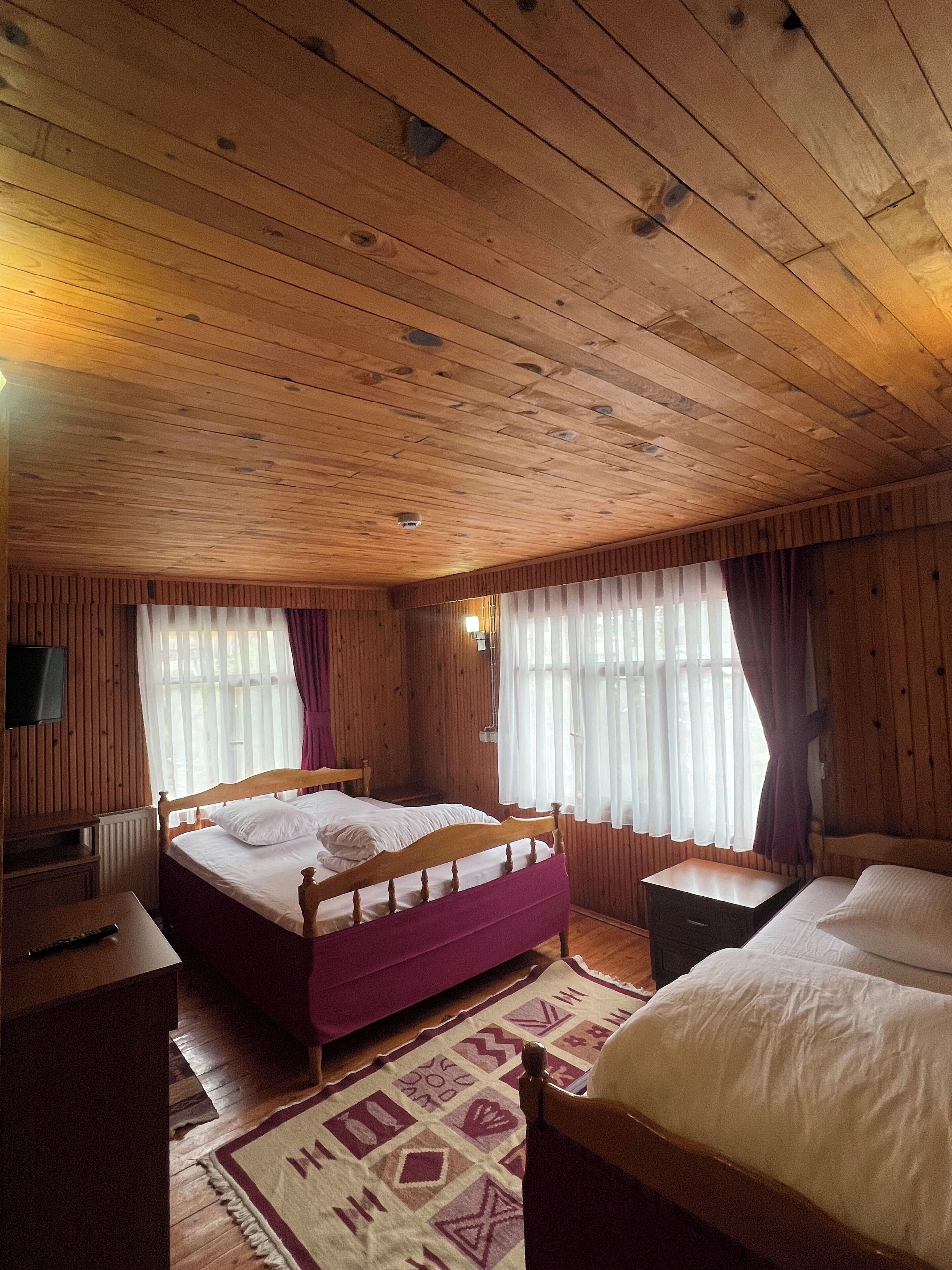 A wooden cabin room with a bed, a bedside table, a chair, and a television on the wall.