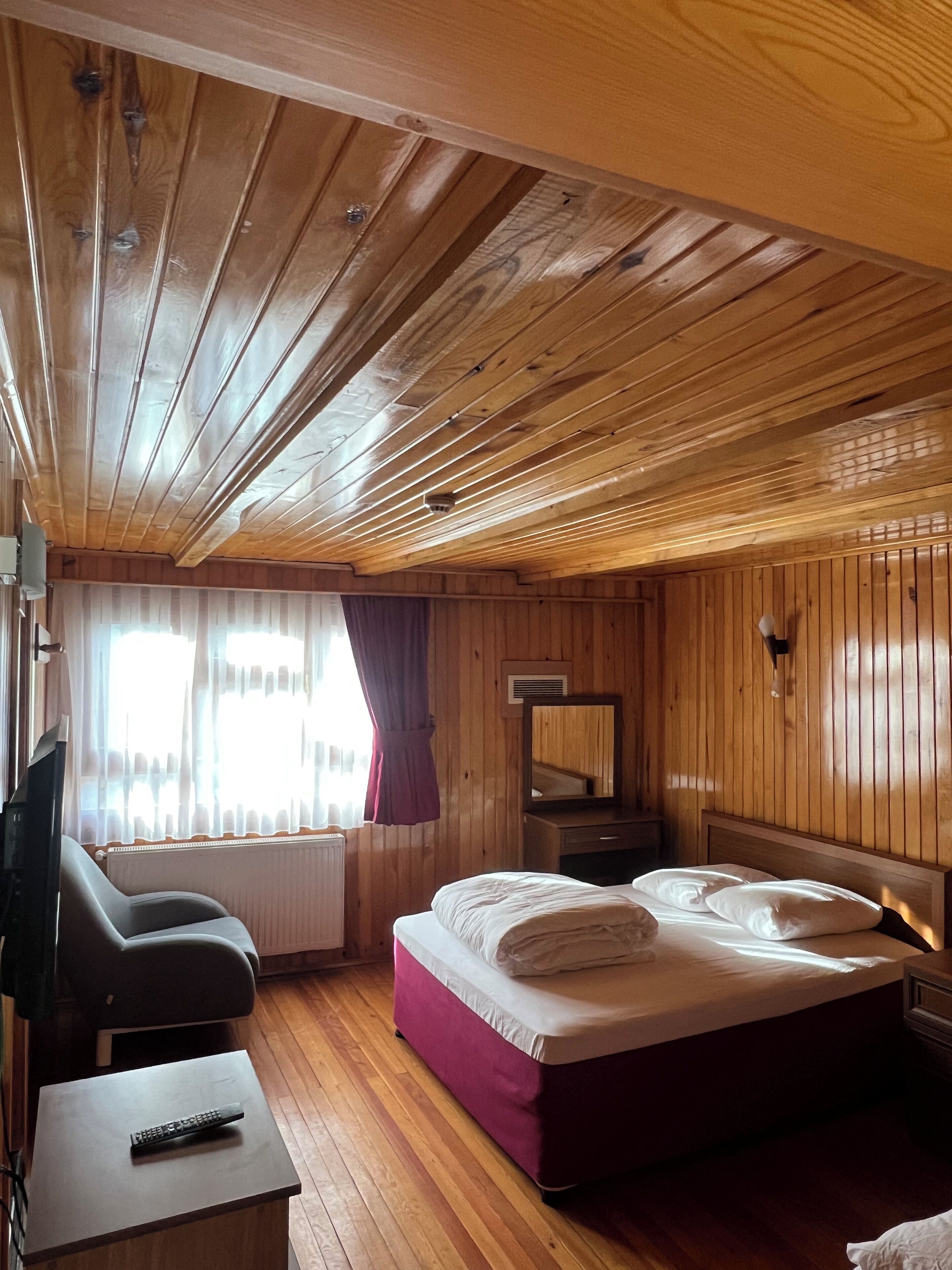 Una stanza con rivestimenti in legno, un letto, una poltrona, un televisore e una finestra con tende.