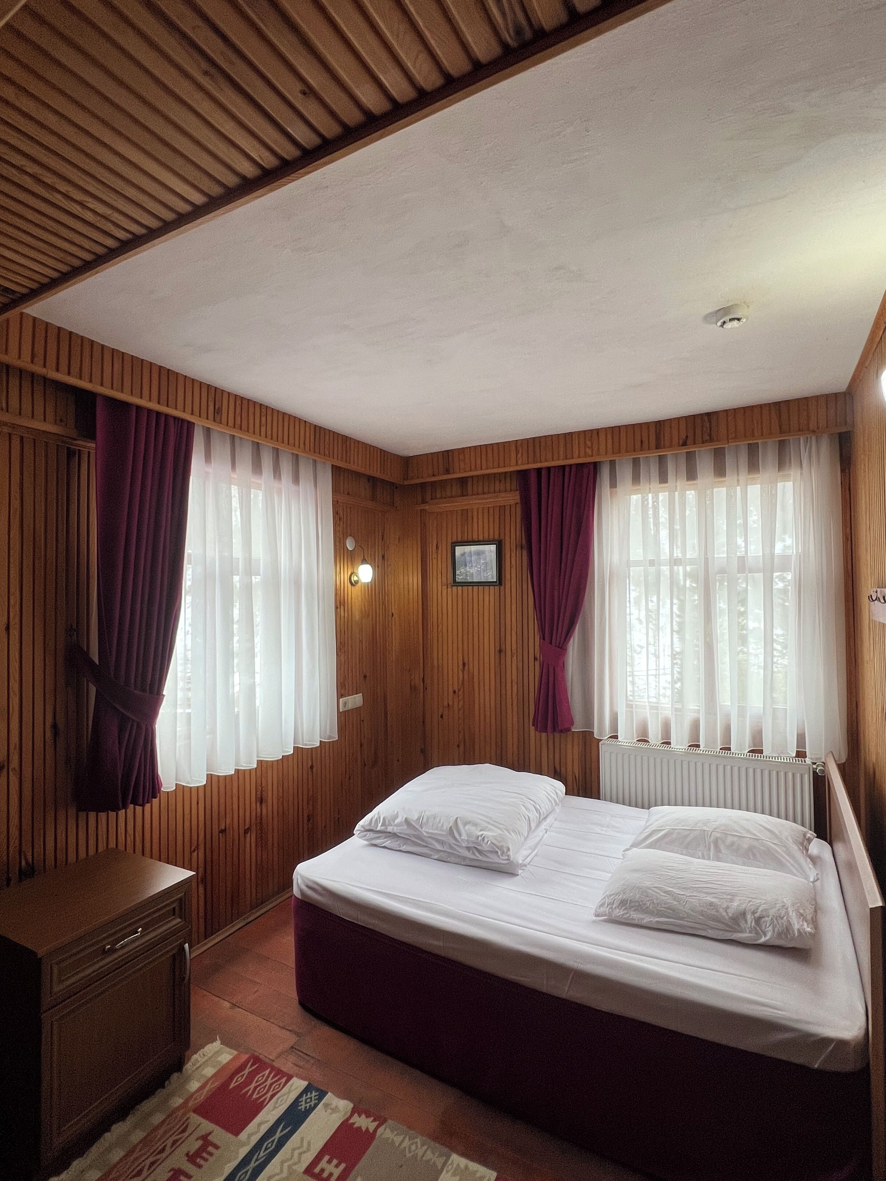 A room with wooden panel walls, a bed with white linens, a wooden dresser, and a radiator.