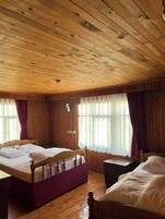 Una habitación con paneles de madera, dos camas, techo de madera y ventanas amplias con cortinas.