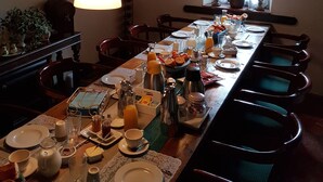 Een lange eettafel gedekt voor het ontbijt, met verschillende gerechten, drankjes en een klok aan de muur.