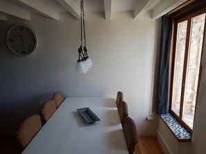 A dining area with a white table, four brown chairs, a hanging light fixture, and a clock on the wall.