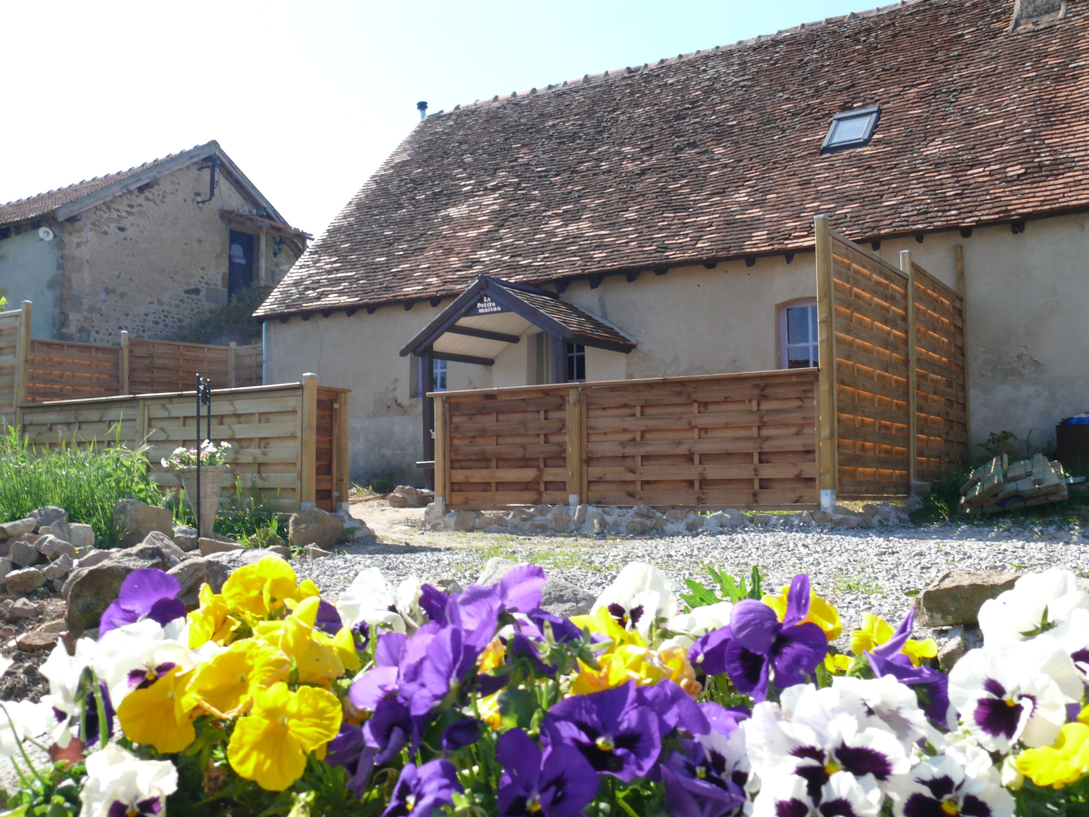 A rustic building with a tiled roof, a wooden gate, and a flower garden in the foreground.