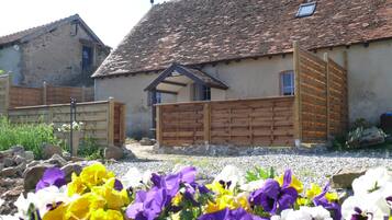 A rustic building with a tiled roof, a wooden gate, and a flower garden in the foreground.