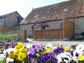 A rustic building with a tiled roof, a wooden gate, and a flower garden in the foreground.