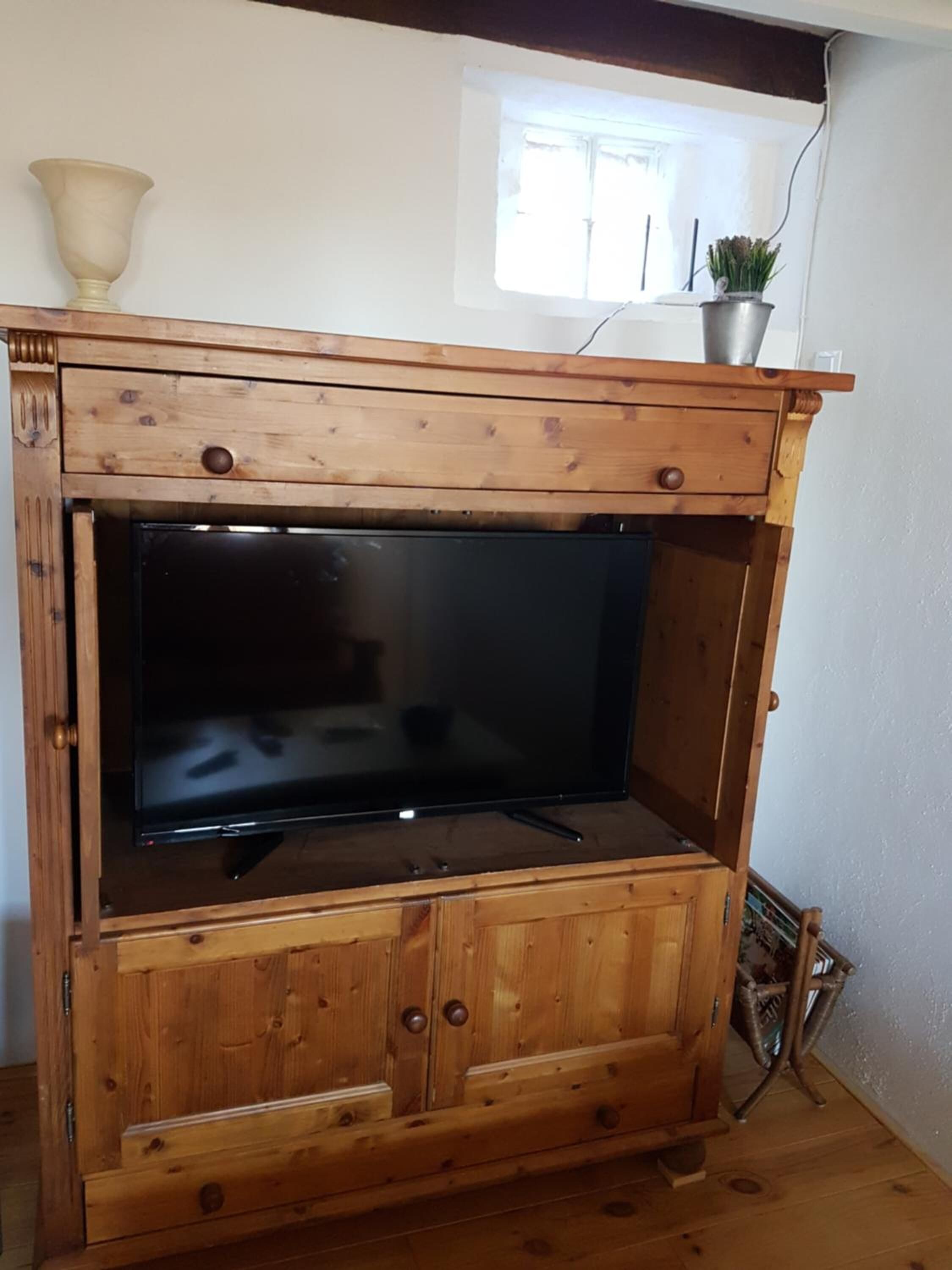 A wooden entertainment center with a flat-screen TV, a small shelf with a potted plant, and a window above.