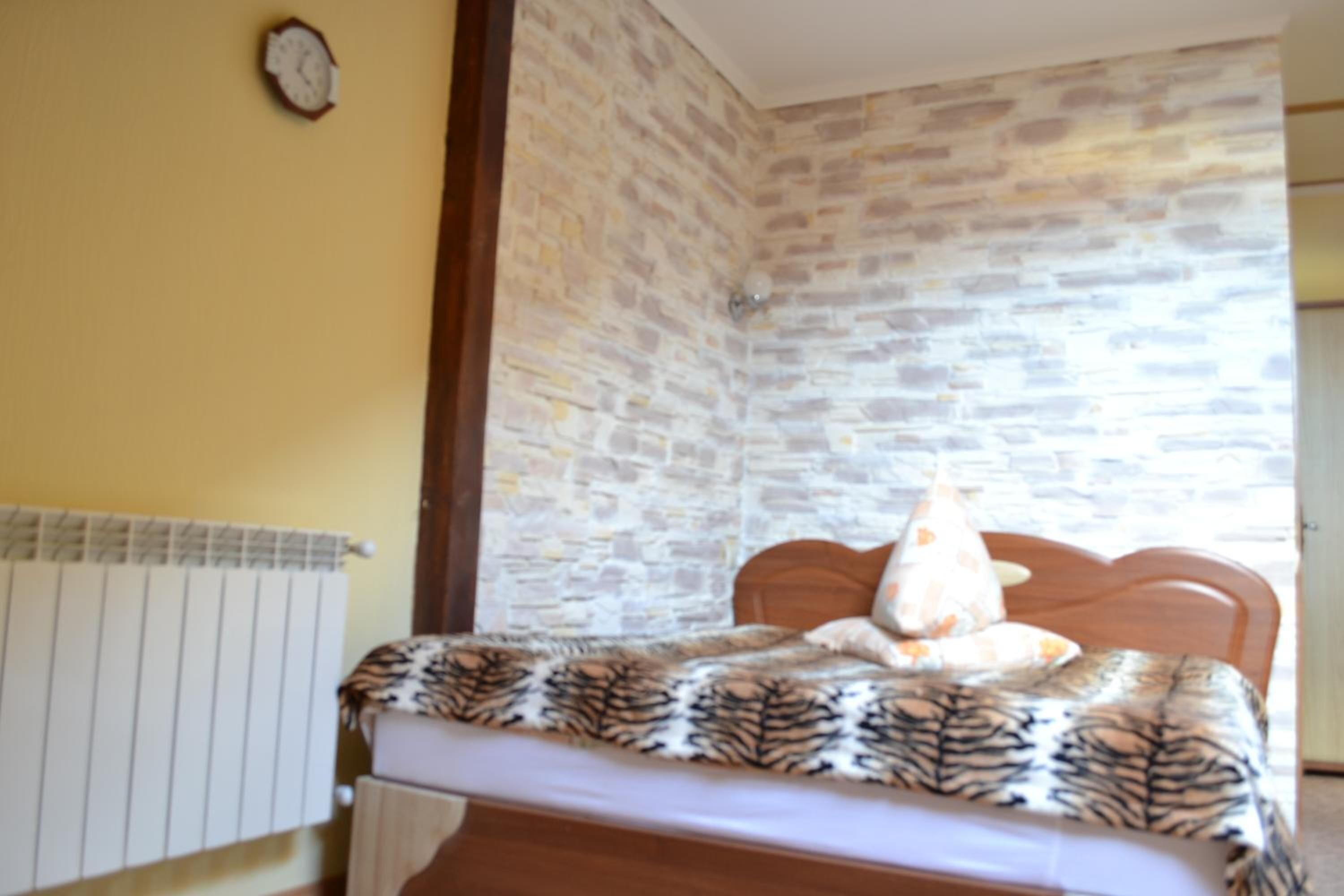 Un dormitorio con cama, cabecera de madera, colcha estampada, radiador y pared de piedra.