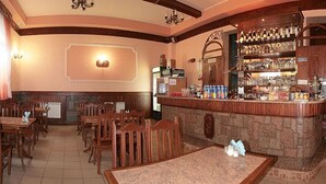 Un restaurant avec des tables et des chaises en bois, un coin bar avec des bouteilles exposées et un mur en pierre.
