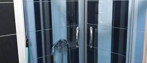 A glass-enclosed shower stall with a handheld showerhead and a wall-mounted faucet.