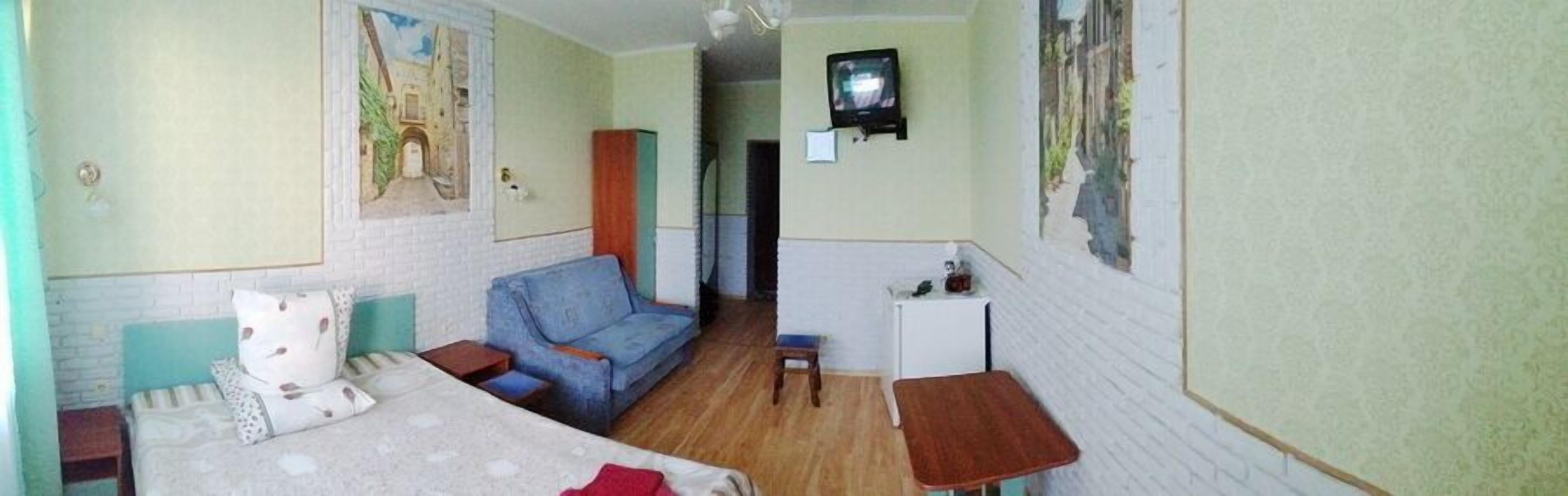 A small, cozy room with a bed, a sofa, a small table, and a television.