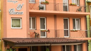 Un immeuble à plusieurs étages doté de balcons, une voiture garée devant, et un jardin agrémenté de fleurs et d’un banc.