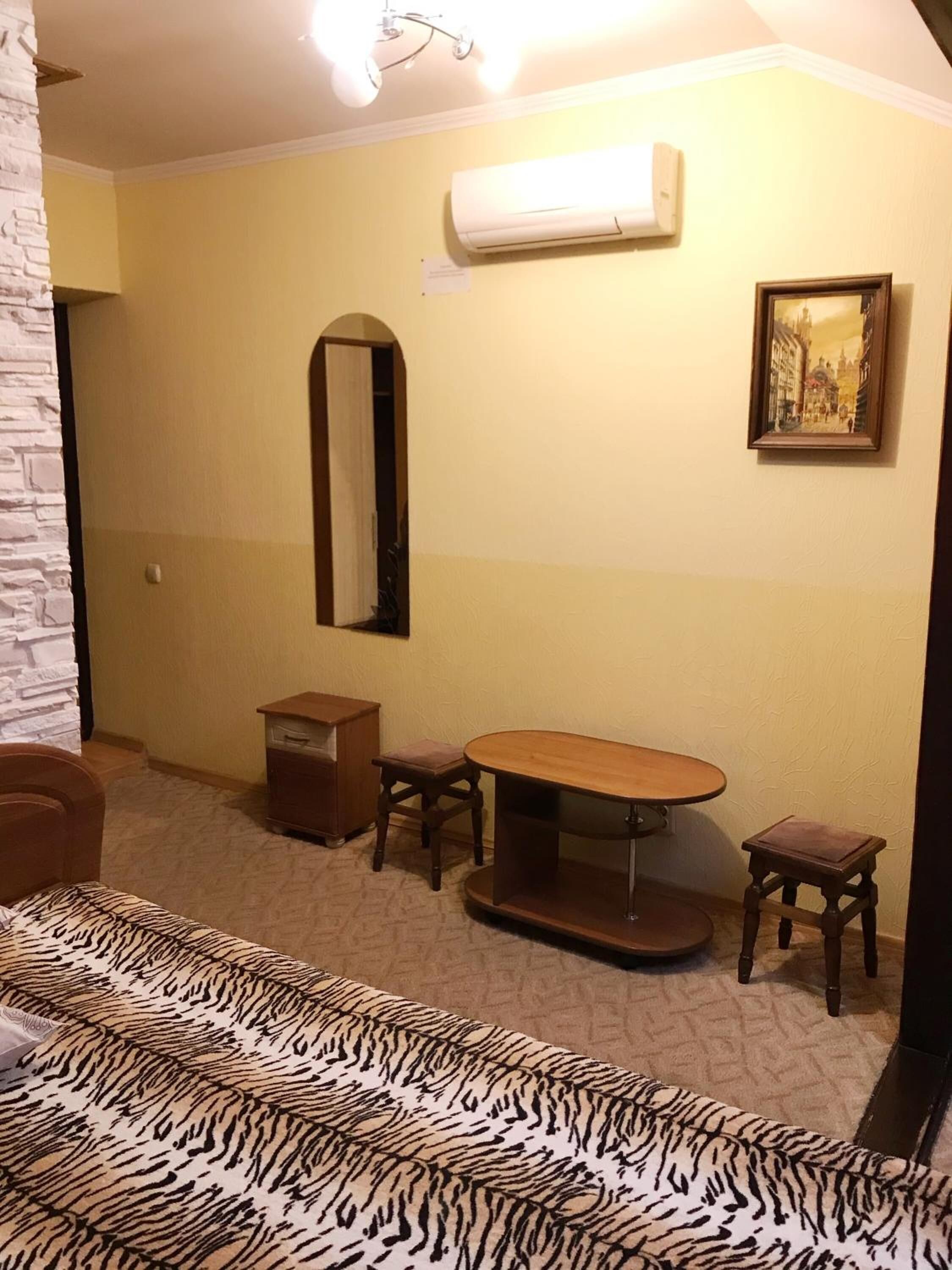 Une pièce comprenant un lit, une table en bois, deux chaises, un petit meuble, un miroir et un appareil de climatisation fixé au mur.
